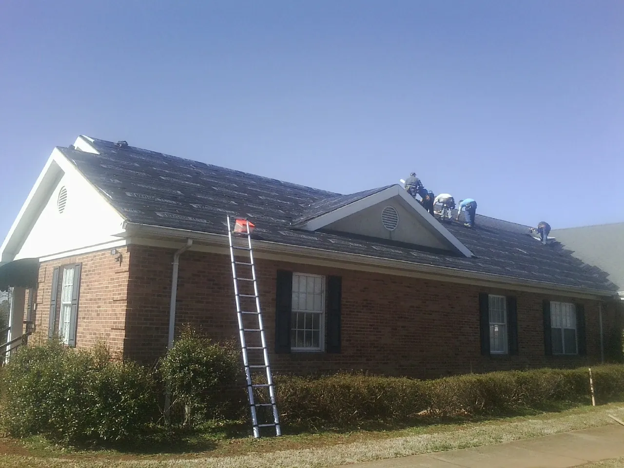 Crew tearing shingles off a brick ranch roof with a ladder set — Emergency Roof Repair work by our crew in Nezperce
