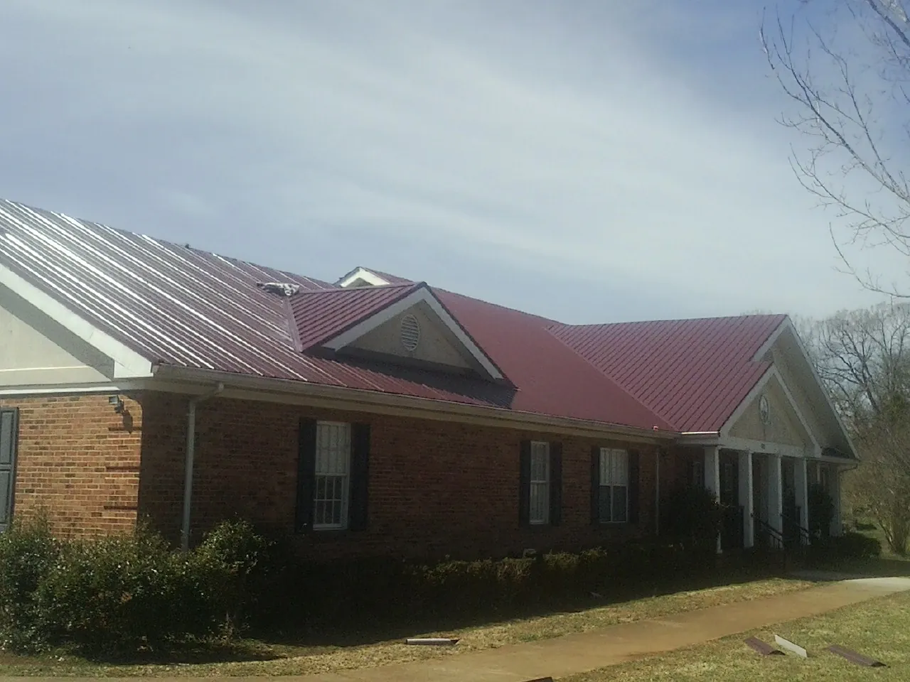 Red metal roof with gabled entries on a long brick building, from a Hail Damage Roof Repair job in Nezperce