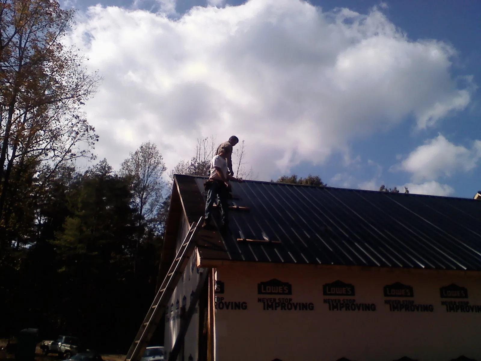 Roofer fastening dark metal panels high against a cloudy sky, from a Roof Inspection job in Nezperce
